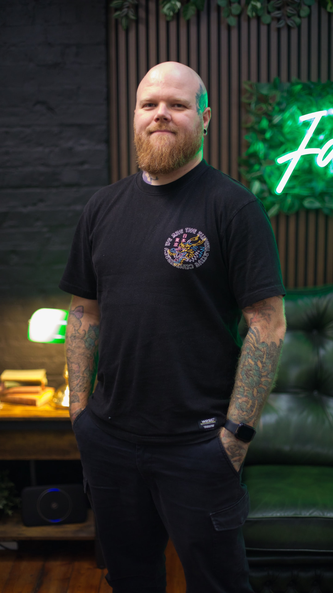 Sam Andrews standing in False Idols Tattoo Studio beside the green neon sign